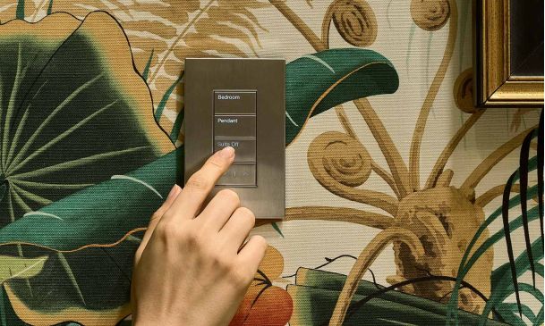 Woman's hand pressing a button on a Lutron palladiom keypad on floral wallpaper
